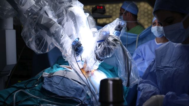 Bild einer robotergestützten Operation mit dem Roboter im Fokus und medizinischem Personal im Hintergrund. Symbolbild für eine Transplantation.
